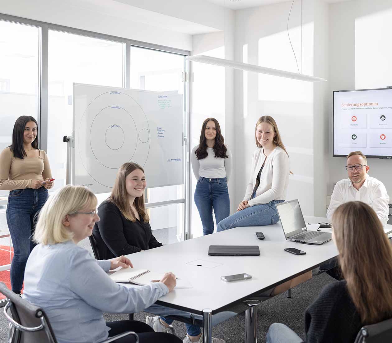 Auszubildende und Angestellte in neugieriger und lockeren Atmosphaere im Büro mit Whiteboard